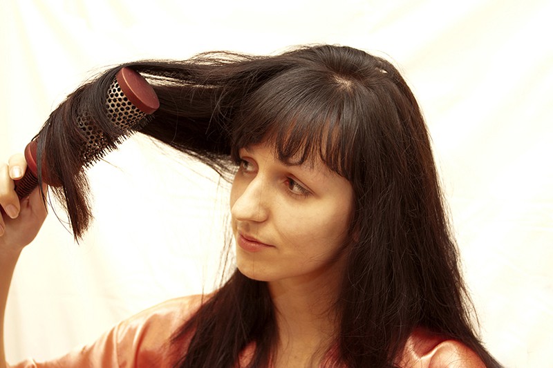 The woman combs hair the hair dryer on a white background