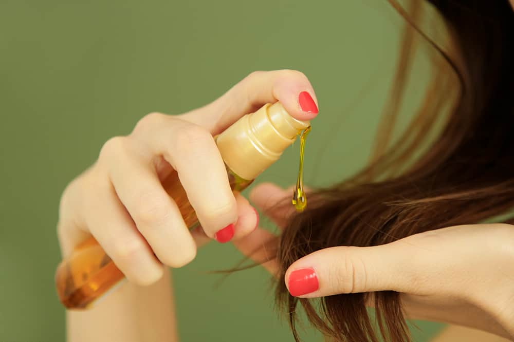 Lady put hair oil on hair to prevent damage