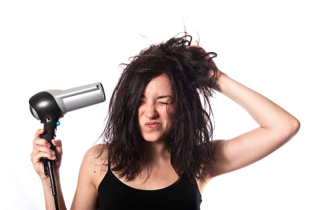 a girl is not happly to blow dry hair with a hair dryer