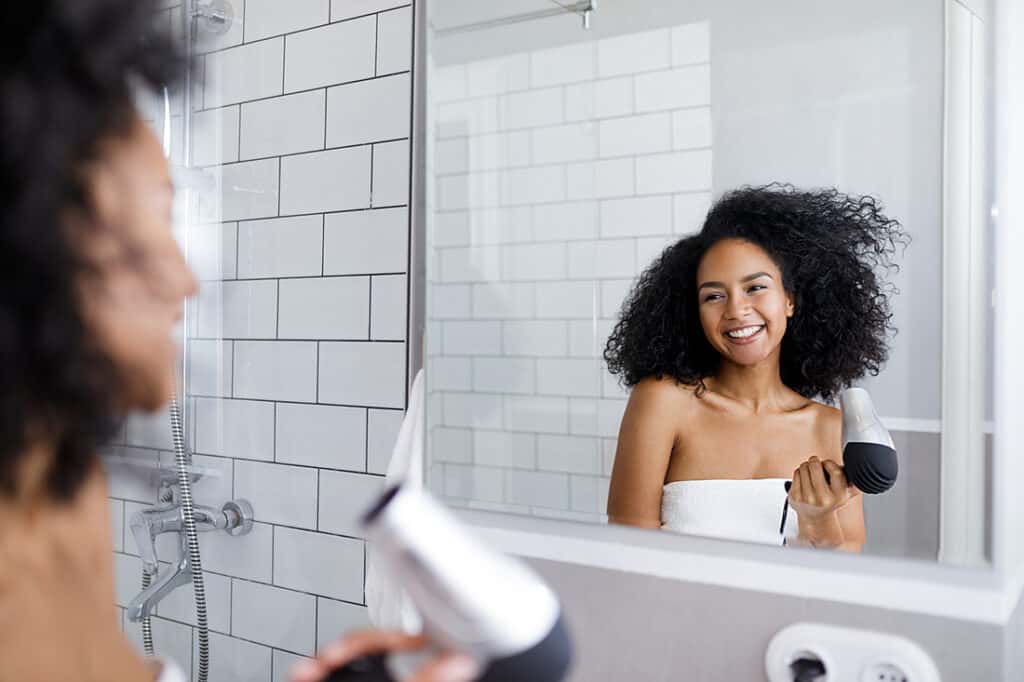 Smiling woman holds a hair dryer,look at mirror, and blow dry curly hair