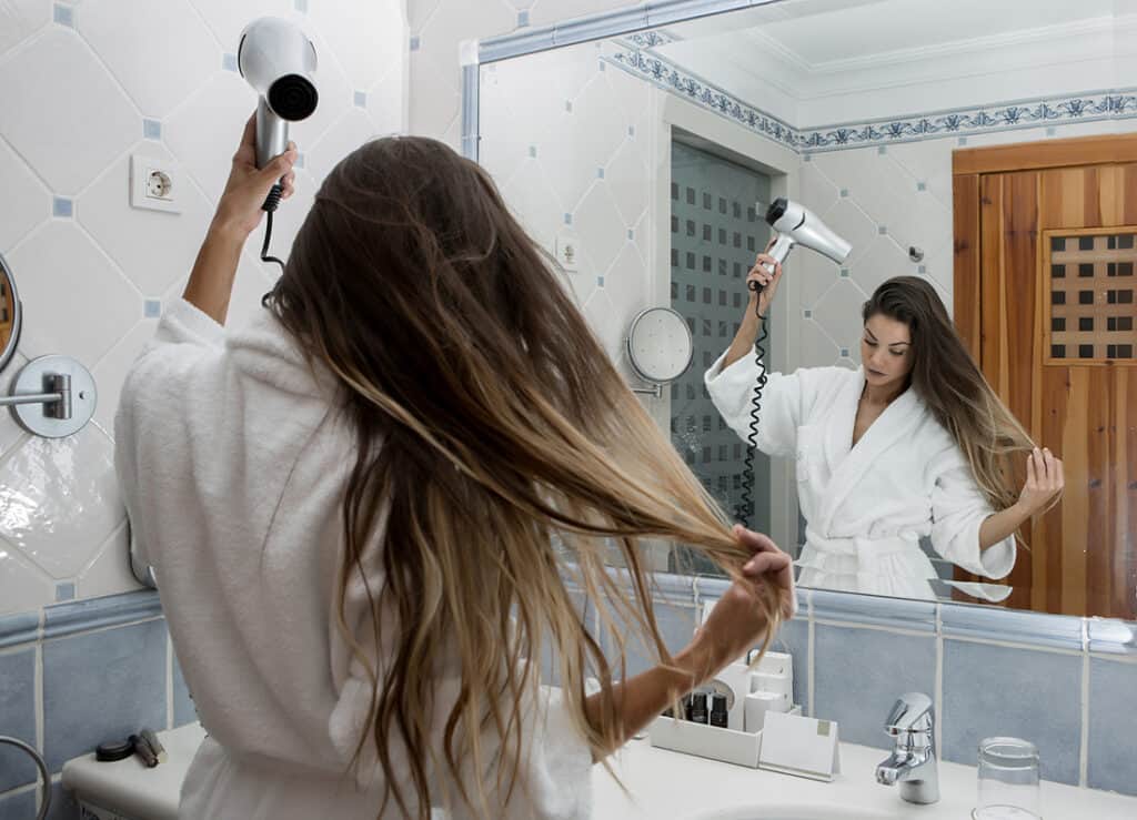 a girl blows dry wet hair in bathroom